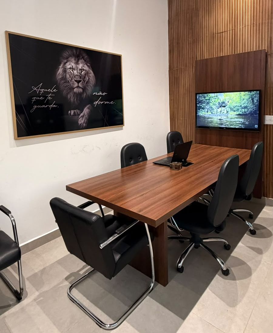 Sala de reuniões com mesa para seis pessoas e televisão